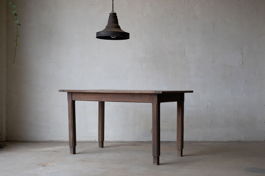 Angled picture of an oak farm table with a rustic finish, a thin tabletop, and a pendant light hanging above.