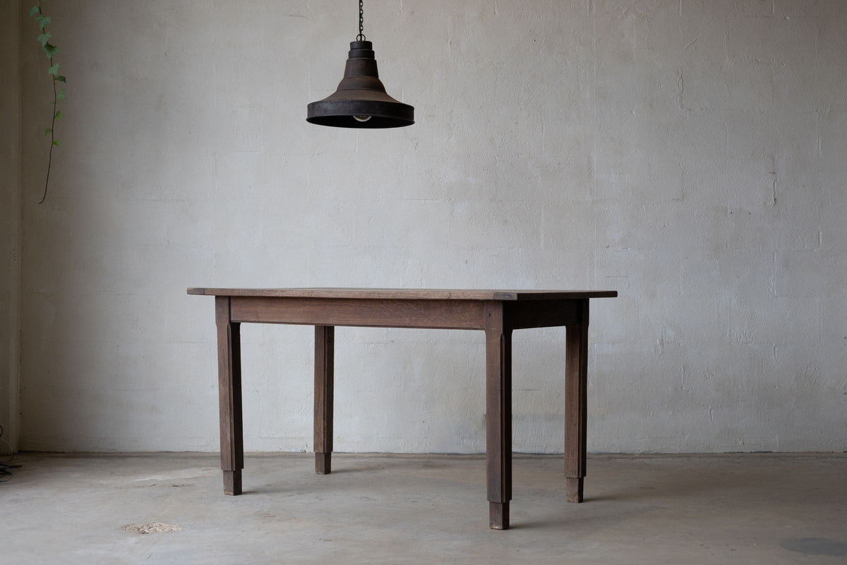 Angled picture of an oak farm table with a rustic finish, a thin tabletop, and a pendant light hanging above.