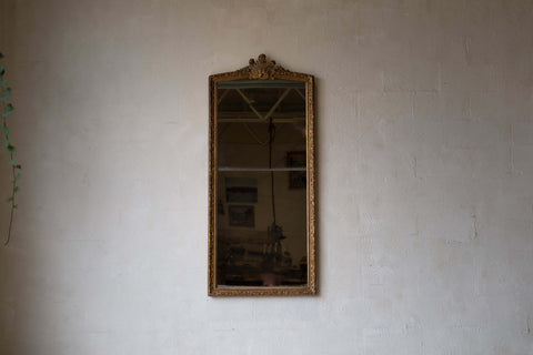 A full-length antique split glass mirror with a baroque gold frame, set against a neutral wall.