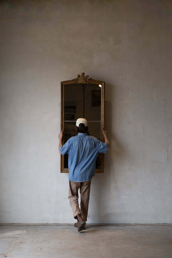 A man holding a full-length antique split glass mirror with an intricate gold frame.