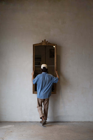 A man holding a full-length antique split glass mirror with an intricate gold frame.