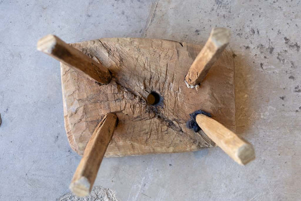 Underside of a small workman's stool, showing mortise and tenon joints and aged wood.
