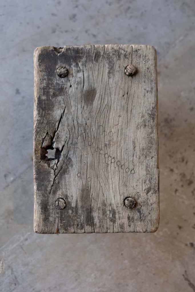 Overhead view of a small, rectangular workman's stool, with aged wood and mortise and tenon joins at each corner. 
