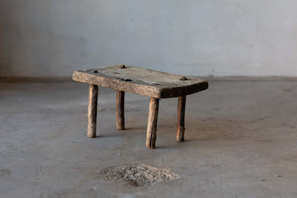 A small, wooden, rectangular workman's stool with rustic legs.