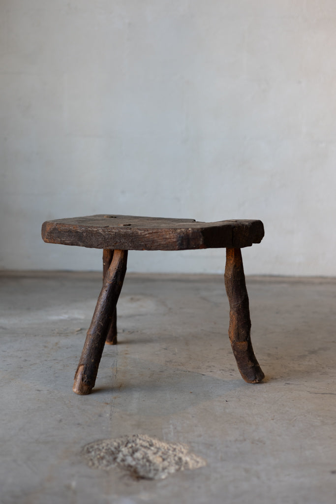 A small, wooden, rectangular workman's stool with three legs.