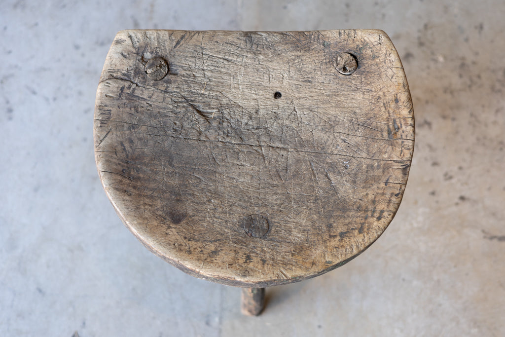 Overhead view of a small, round workman's stool, with aged wood.