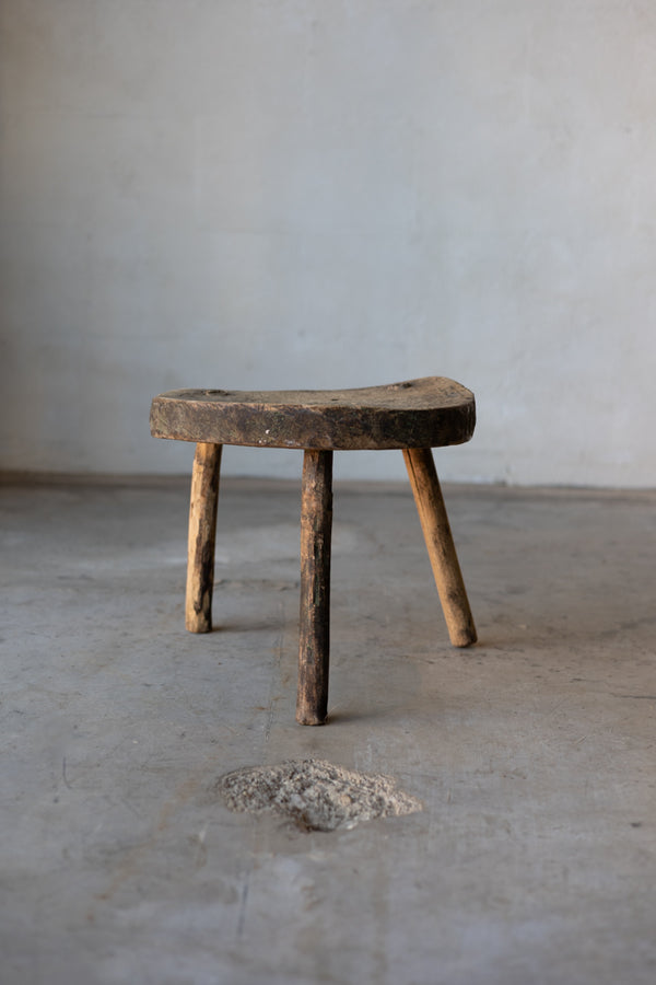 A small, wooden, workman's stool with rustic legs.
