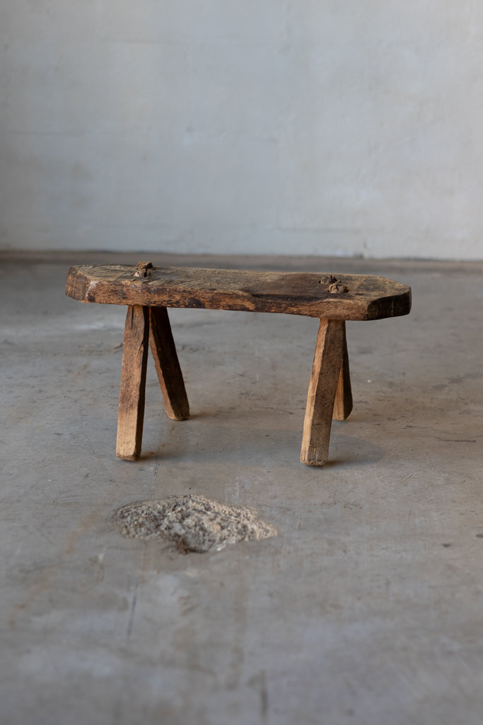 A small, wooden, rectangular workman's stool with rustic legs.