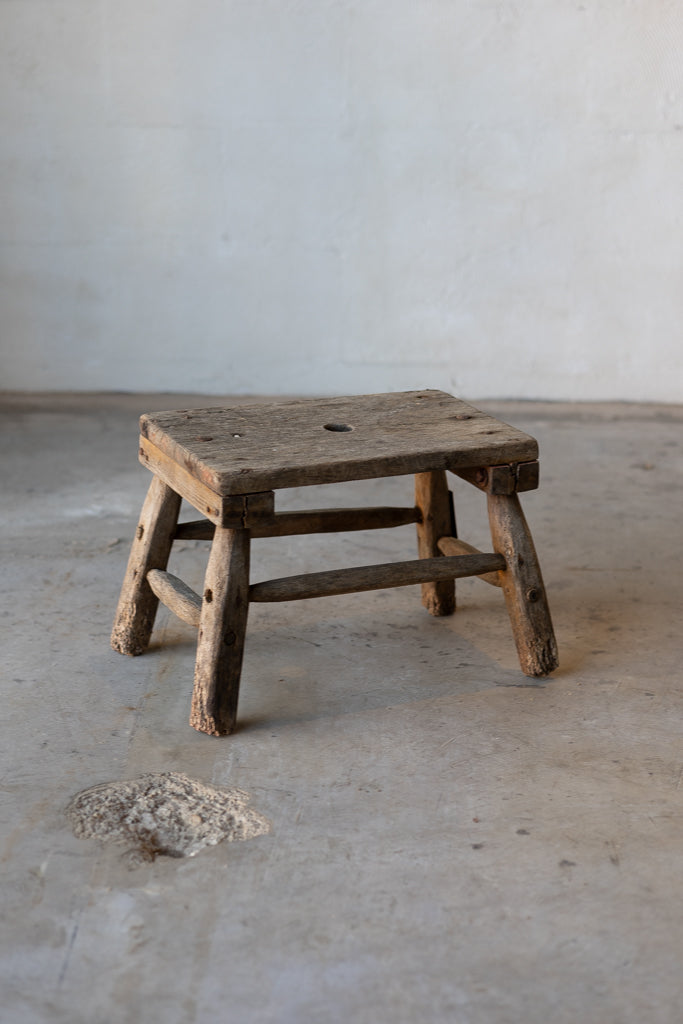 A small, wooden, rectangular workman's stool with rustic legs.