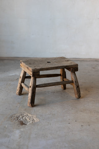 A small, wooden, rectangular workman's stool with rustic legs.