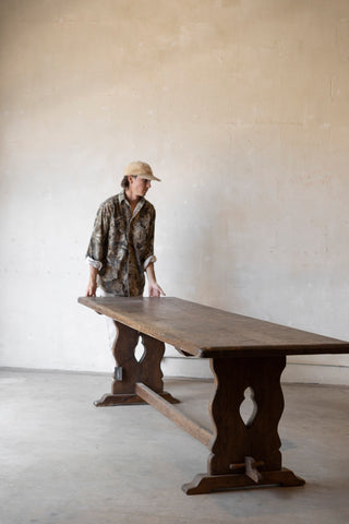Person standing next to a large wooden table in a minimalistic room.