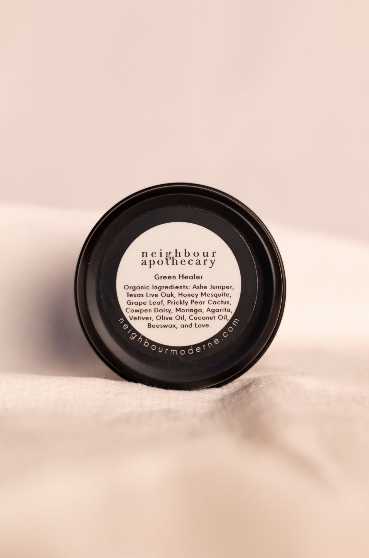 Neighbour Apothecary all natural ashe juniper moisturizing balm ingredient label on the bottom of the container on a soft white background.