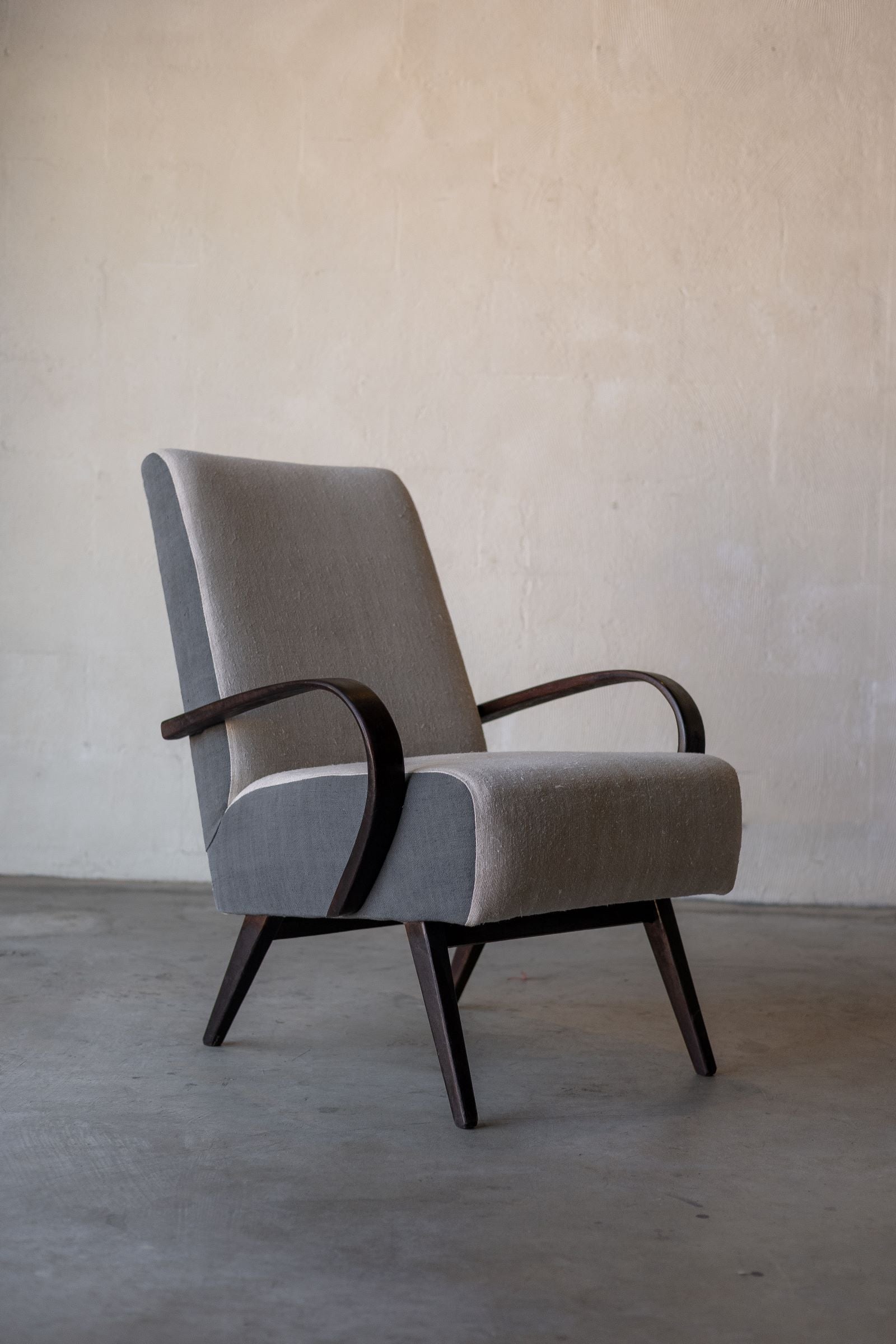 Hero photo of vintage Halabala lounge chair with curved wooden armrest and wooden legs, featuring cream linen reupholstery on backrest and seat.