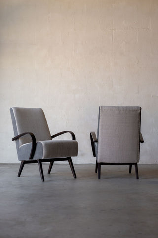 Contrasting angles of a pair of vintage Halabala lounge chairs facing each other, featuring cream linen reupholstery on backrest and seat, and grey linen on chair's sides.
