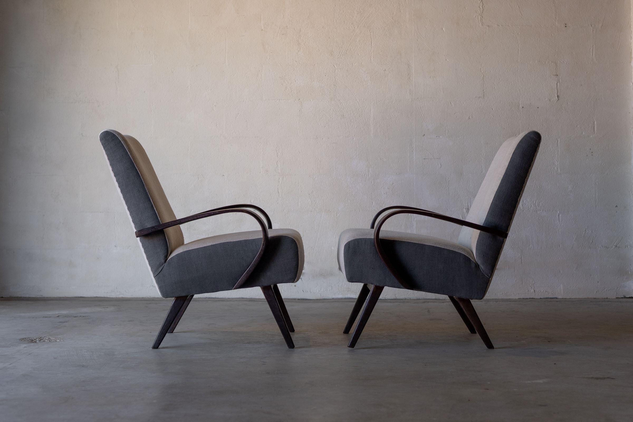 Profile view of pair of vintage Halabala lounge chairs facing each other, featuring cream linen reupholstery on backrest and seat, and grey linen on chair's sides.