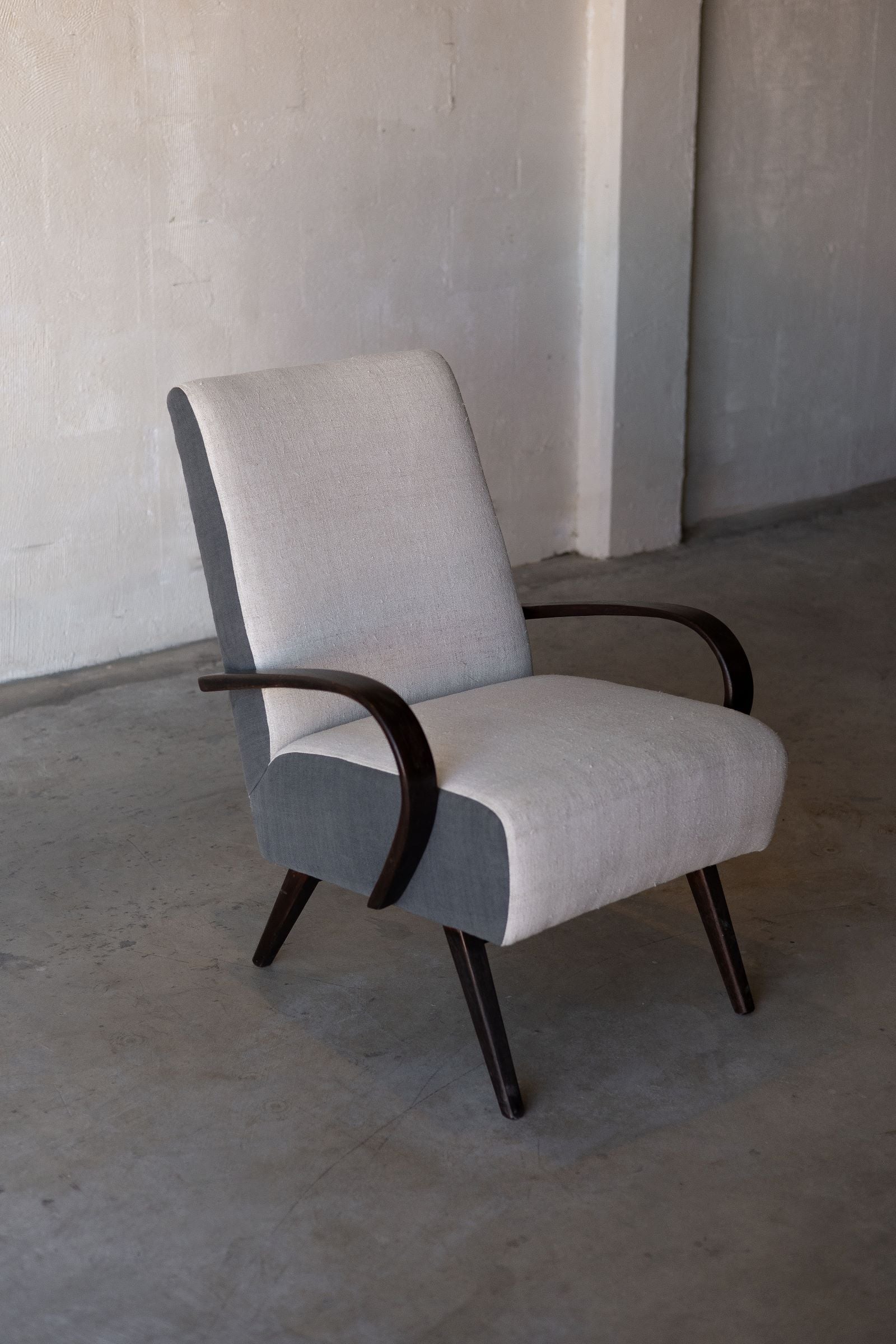 Side angle photo of vintage Halabala lounge chair with curved wooden armrest and wooden legs, featuring cream linen reupholstery on backrest and seat.