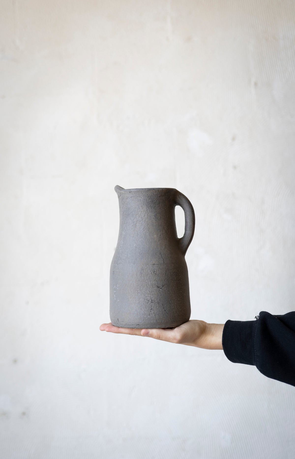 Person holding a gray ceramic pitcher against a plain background