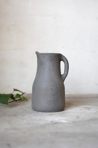 Gray ceramic pitcher on a light surface with a white background