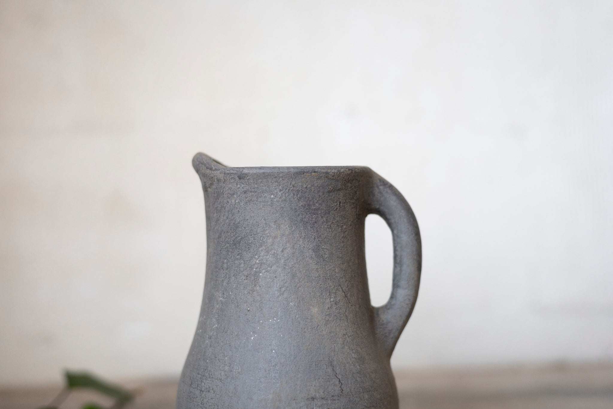 Close-up of a gray ceramic pitcher on a light surface with a white background