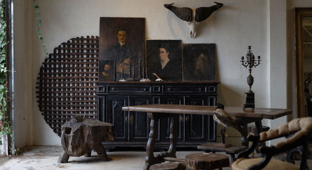 Vintage decor in a well lit room featuring a dark sideboard with candles and vintage portraits and a collection of other pieces. 