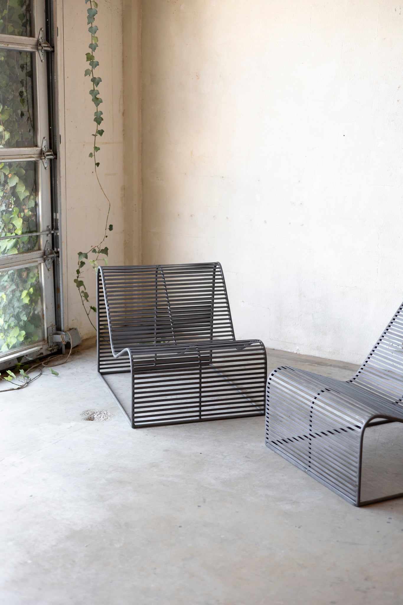 Modern metal chairs in a minimalistic room with a window and plant.