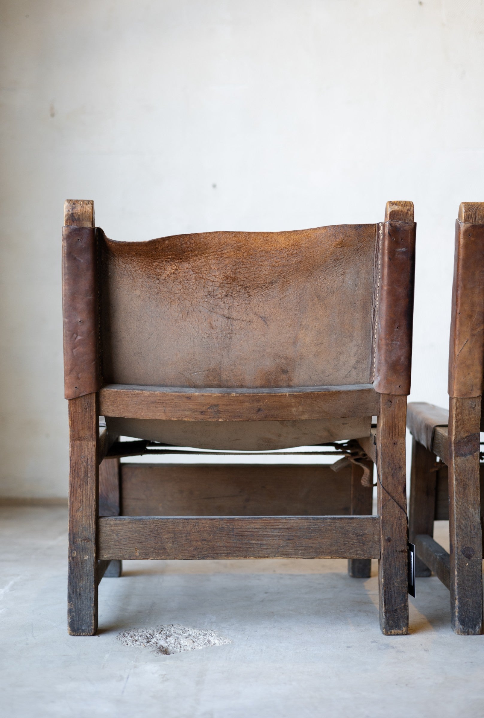 Back of vintage leather and wood sling chair with leather seat in a minimalistic setting.