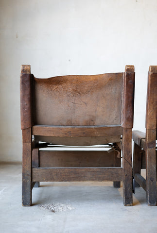Back of vintage leather and wood sling chair with leather seat in a minimalistic setting.