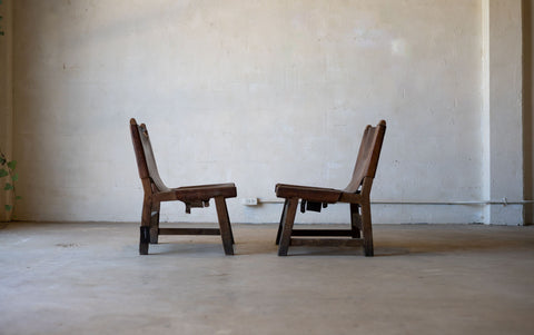 Two vintage wooden sling chairs facing each other in a minimalistic room with a plain wall and floor.