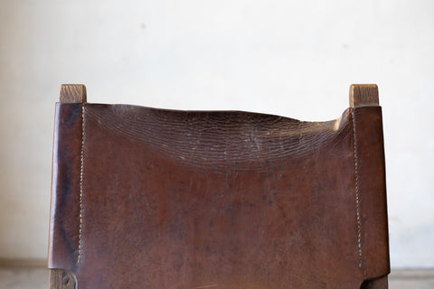 Worn down brown leather sling chair back with wooden frame on a white background.