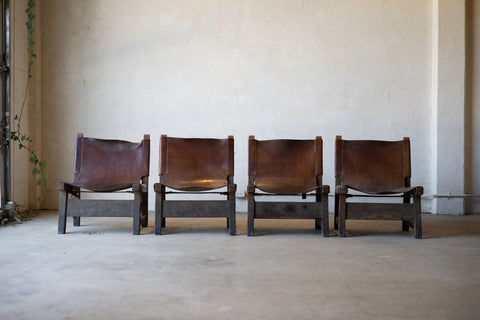 Four vintage brown leather sling chairs lined up against a plain wall.