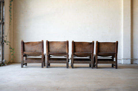 Back side of four vintage brown leather sling chairs lined up against a plain wall.