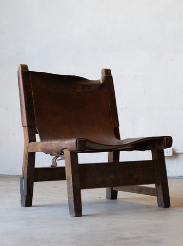 Vintage brown leather sling chair on a light wooden floor with a white wall background