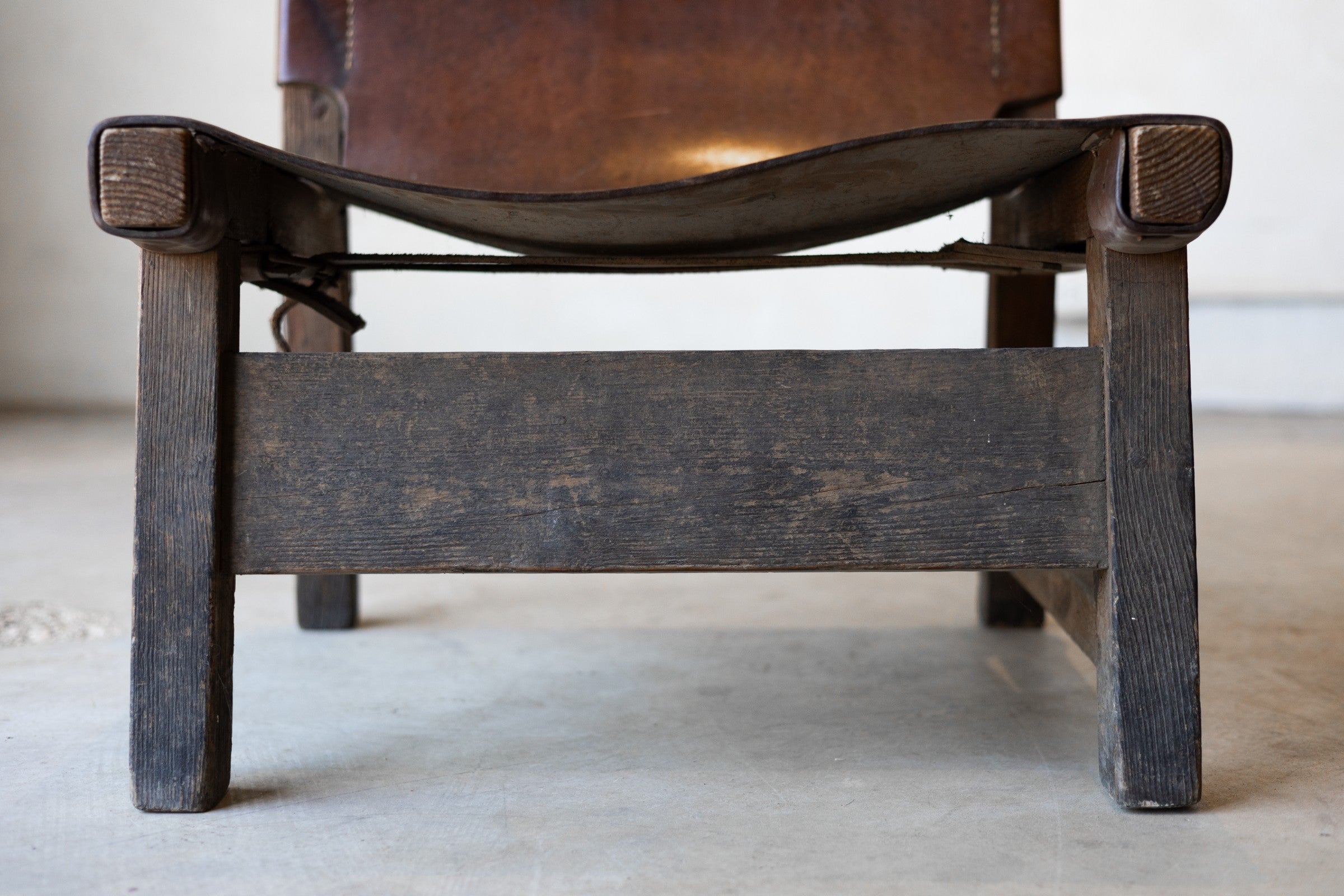 Close-up of the legs of vintage wooden chair with a leather sling seat on a light background.