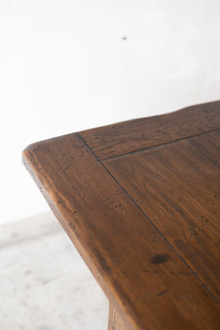 Close-up of a rustic wooden table corner showing the rich brown wood grain and live-edge tabletop against a bright white wall.