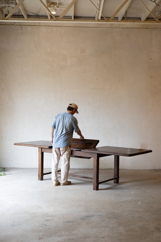 long dark wood dining table in a minimalist room with a concrete floor and plaster wall.