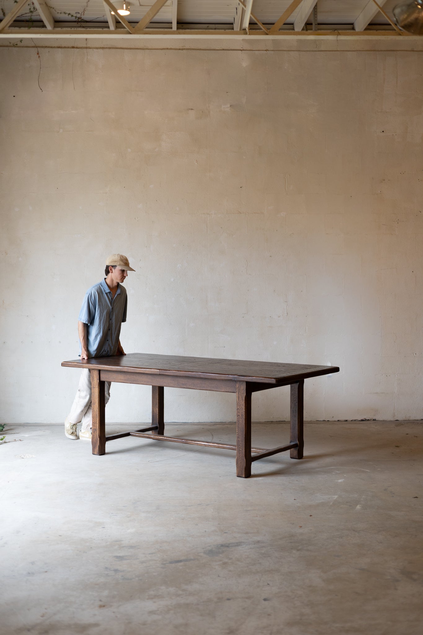 large dark wooden table in a minimalist, industrial-style room with concrete floors and a plaster wall.