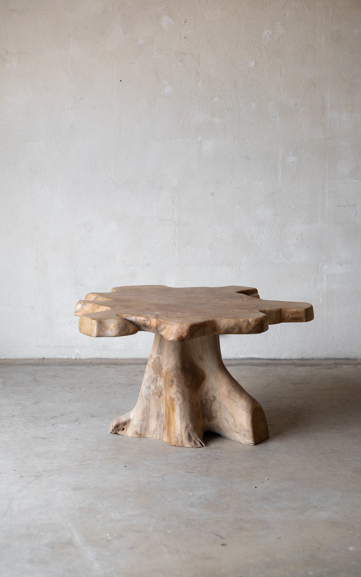 Wooden table with a natural, tree-stump-like base on a plain floor. Main image