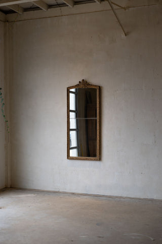 Angled photo of full-length antique split glass mirror with a baroque gold frame, set against a neutral wall.