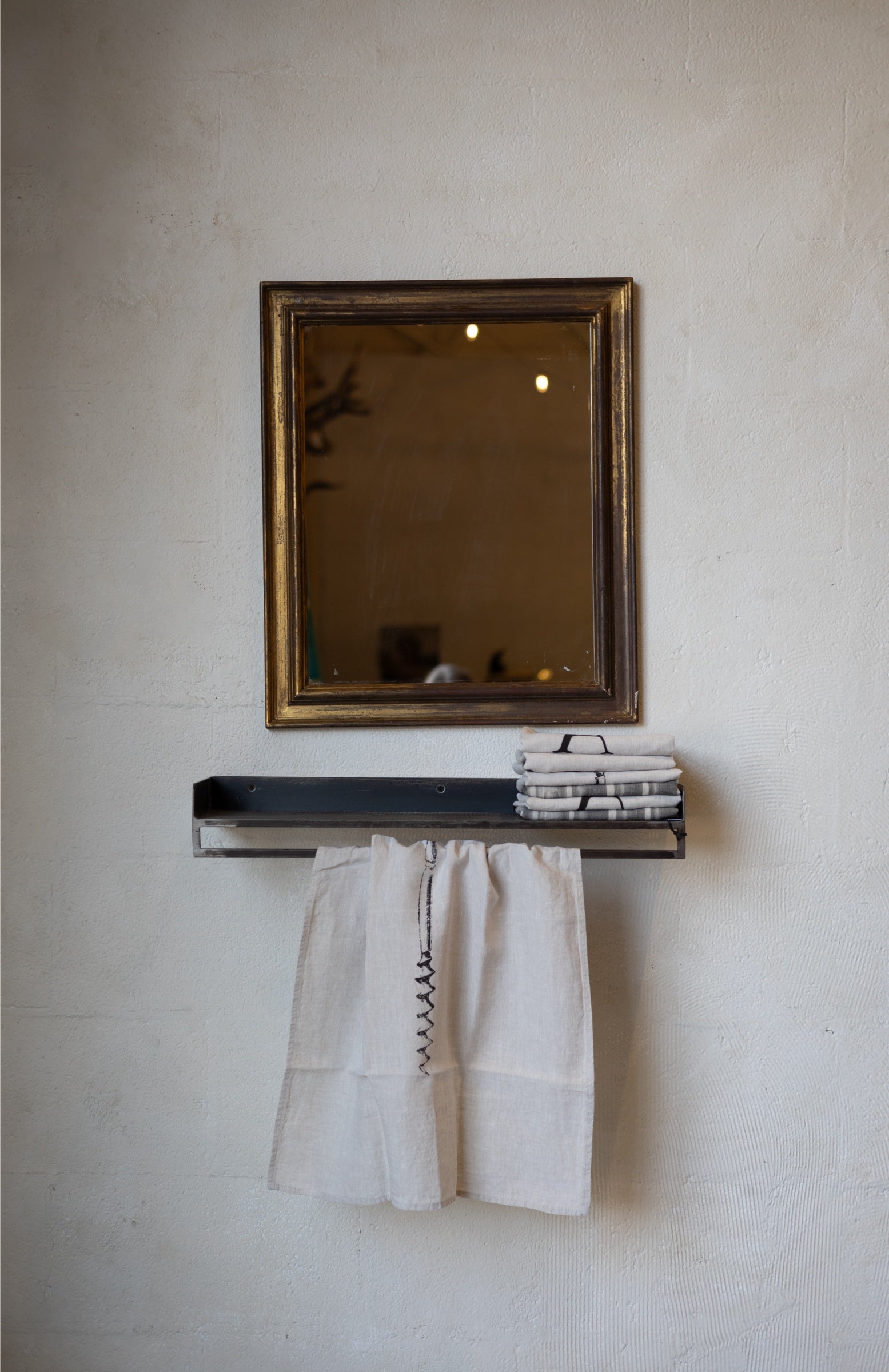 Compact metal shelf with with folded and hanging linens and a mirror on a textured wall