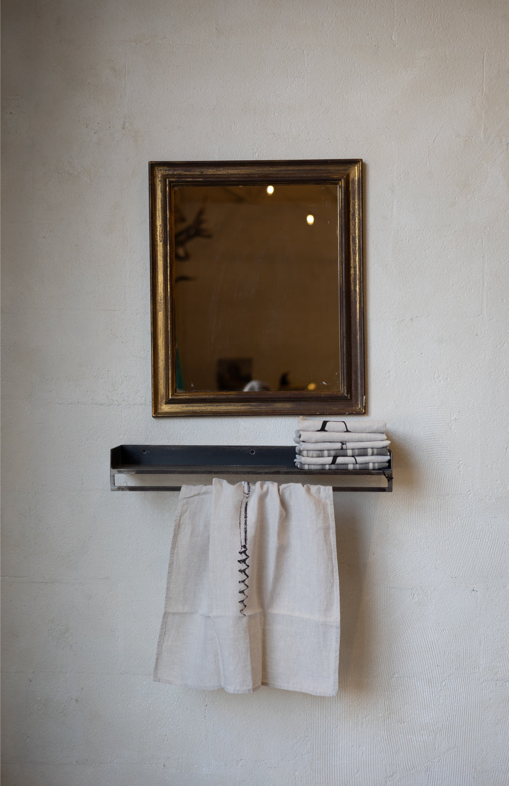 Compact metal shelf with with folded and hanging linens and a mirror on a textured wall