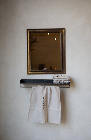 Compact metal shelf with with folded and hanging linens and a mirror on a textured wall