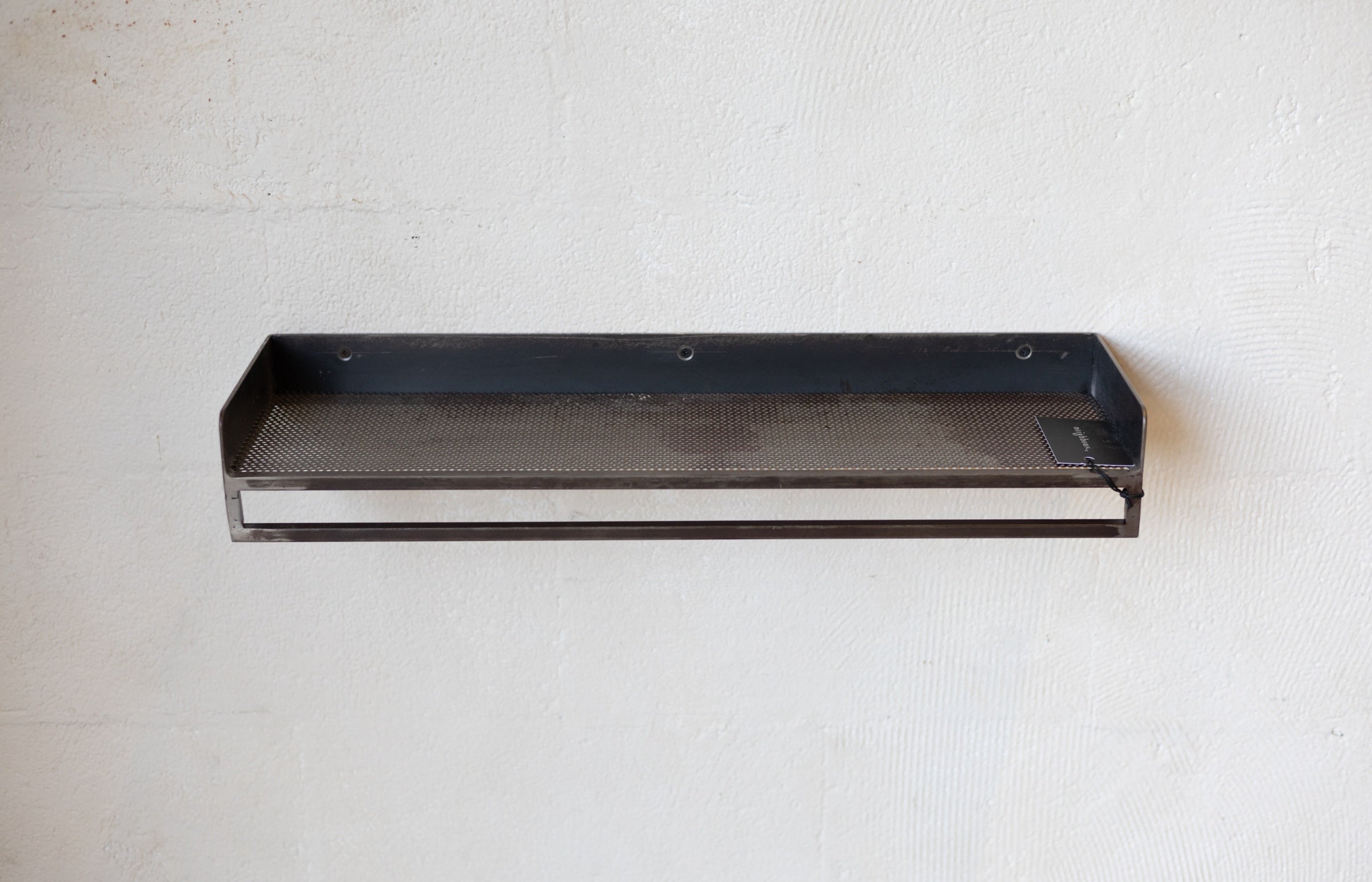 Black metal rack with mesh shelf on a white wall.