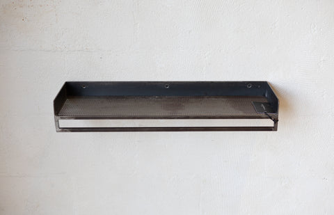Black metal rack with mesh shelf on a white wall.