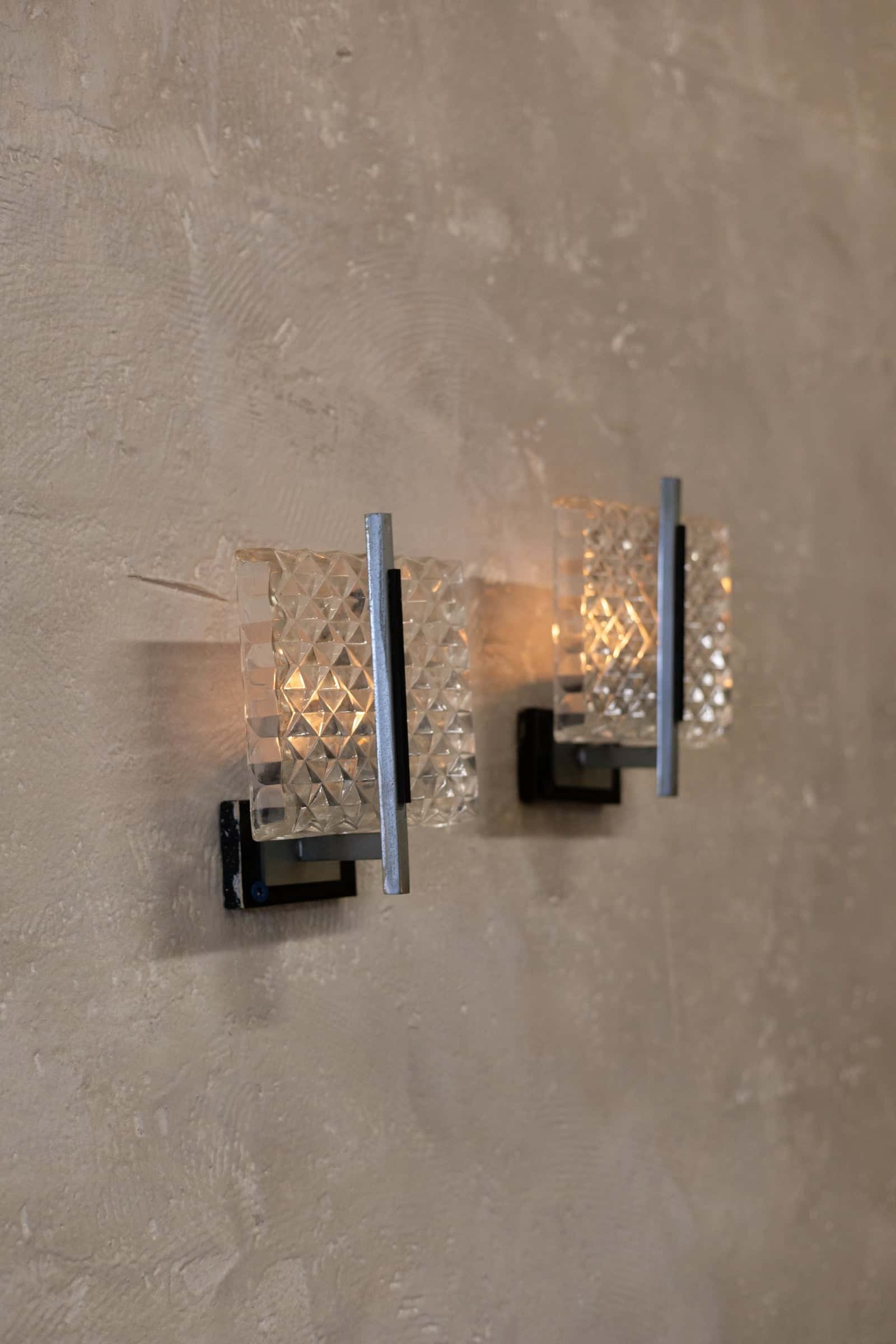Staggered pair of vintage wall sconce featuring a prism glass shade with a diamond pattern and sleek metal frame with a minimalist design.