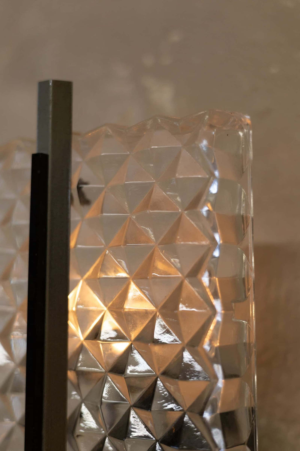 Close-up up vintage wall sconce featuring a prism glass shade with a diamond pattern and sleek metal frame with a minimalist design.