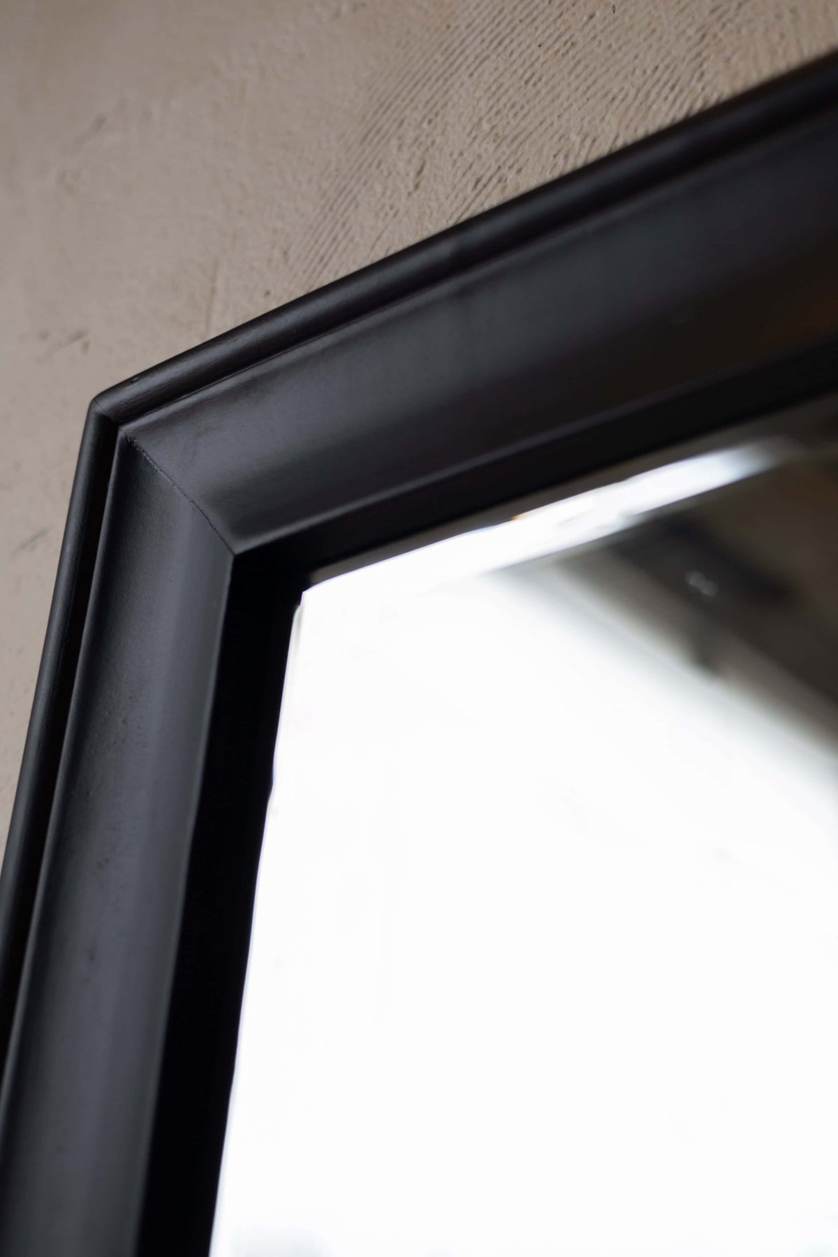 Close-up of mirror's corner, showing black wooden frame with beveled edge.