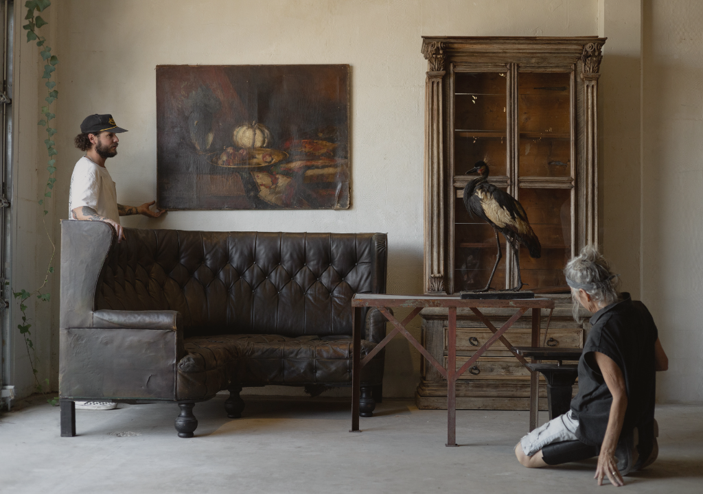 Two men in a room with a leather sofa, wooden cabinet, and painting on the wall.