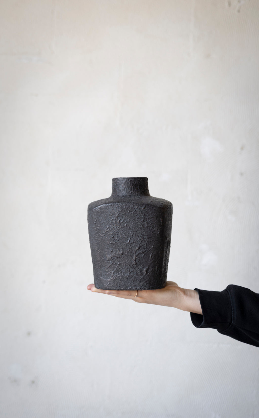 Person holding a textured black vase against a light background