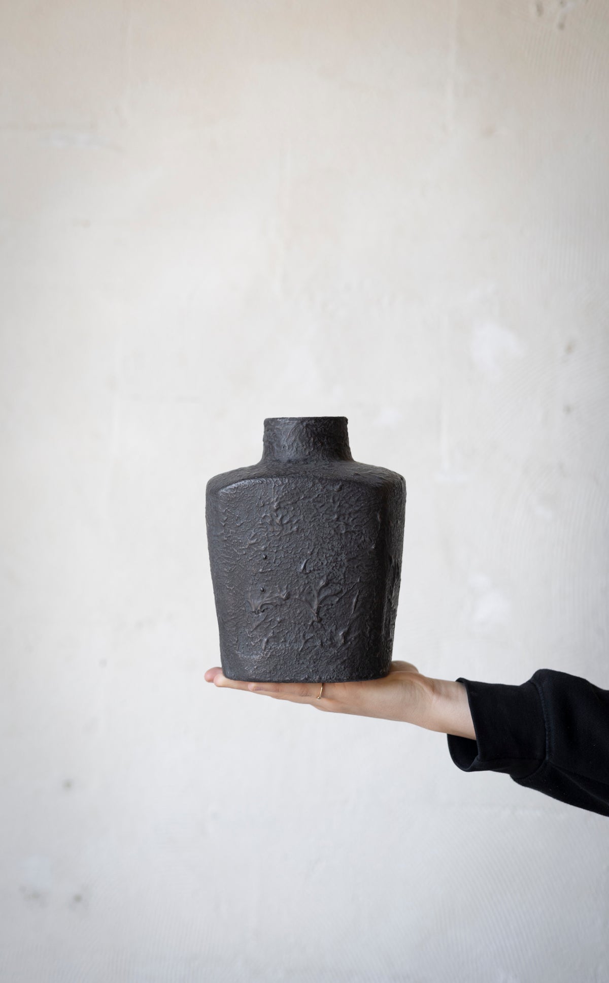 Person holding a textured black vase against a light background