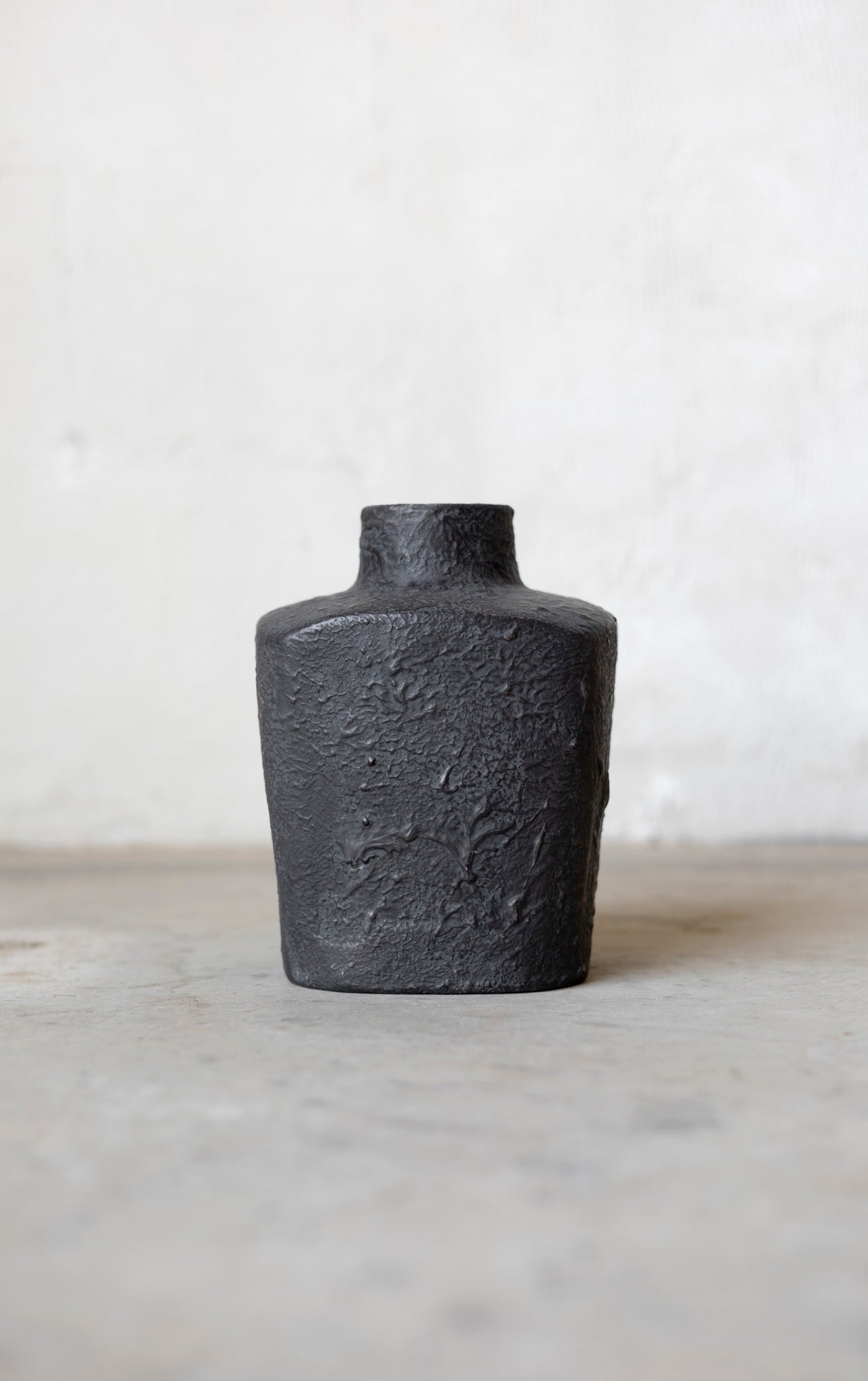 Black textured vase on a light gray surface with a white background